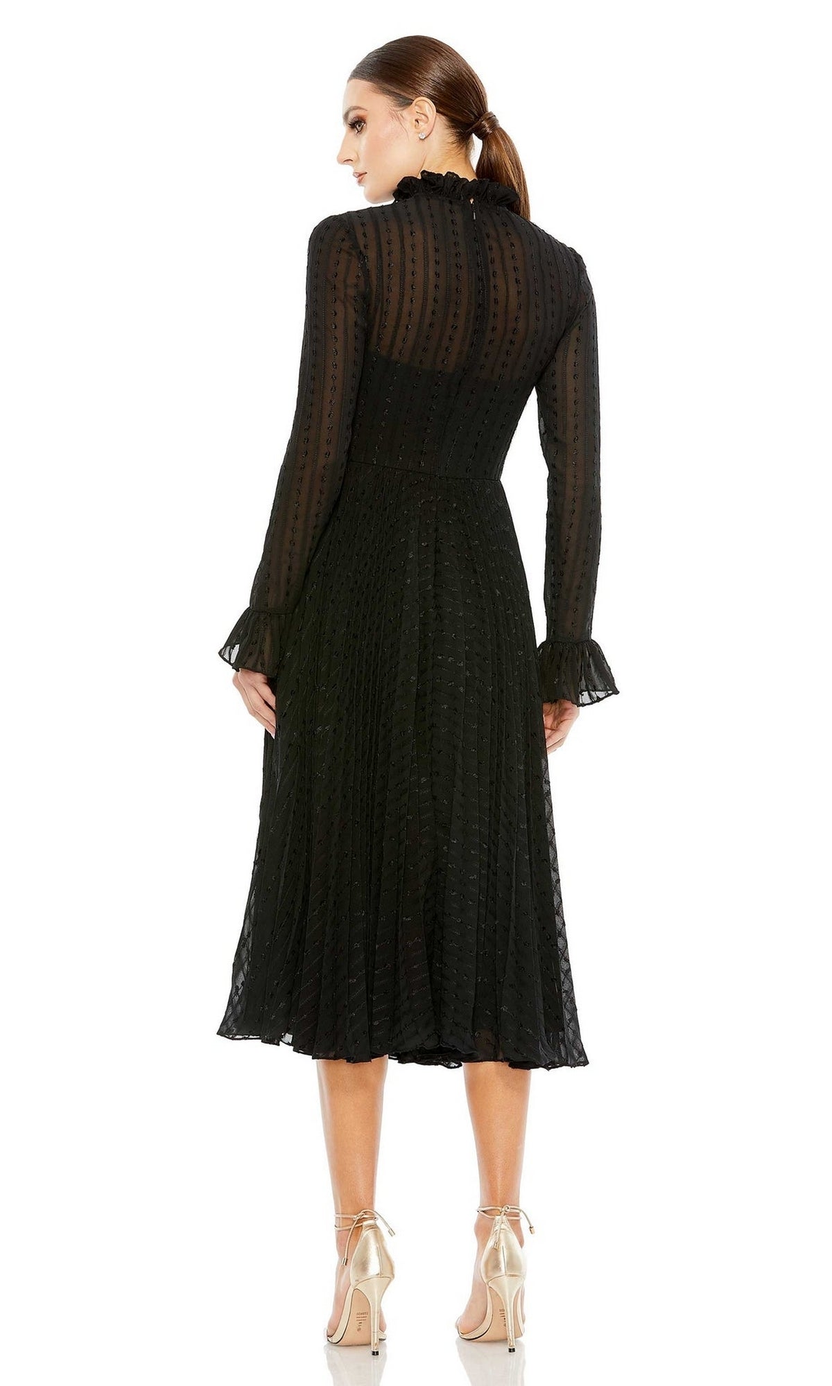 A woman stands with her back to the camera, her hair tied back, wearing the Mac Duggal Short Wedding Guest Dress 49627— a black long sleeve dress featuring sheer dotted fabric and a high neck, styled with nude high-heeled shoes.